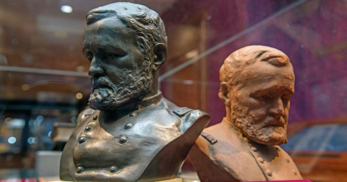 Two busts of a historical figure, one in bronze and the other in terracotta, displayed in a glass case.