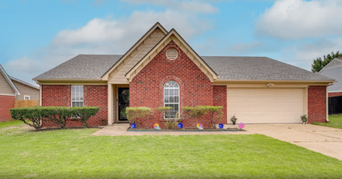 A brick house with a gabled roof, front yard, and colorful decorations along the walkway.