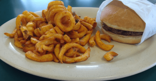 A plate with curly fries and a hamburger wrapped in paper.