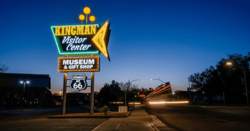 Neon sign for Kingman Visitor Center, Museum & Gift Shop, illuminated at dusk along Route 66.