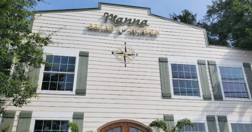 Exterior of a building with the sign "Manna Bread & Heaven" and a compass rose, featuring green shutters and large windows.