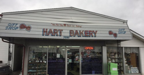 A storefront of Hart Bakery with a sign that reads "We Put The Heart Back Into Baking" and an open sign.