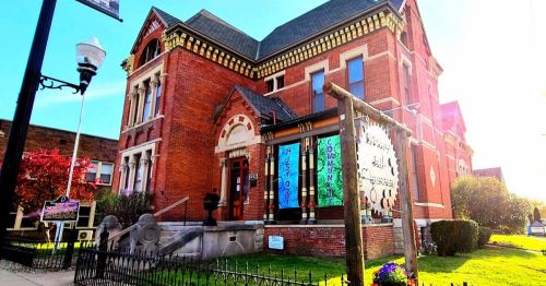 Historic red brick building with decorative architecture, featuring colorful banners and a well-maintained garden.