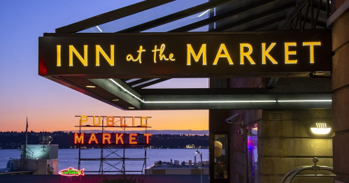 Sign for "Inn at the Market" with a view of the "Pike Place Market" sign at sunset over the water.