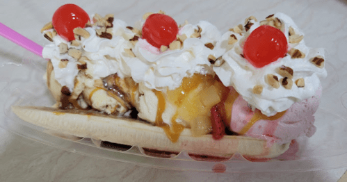 A banana split topped with whipped cream, cherries, nuts, and various sauces, served in a clear dish.