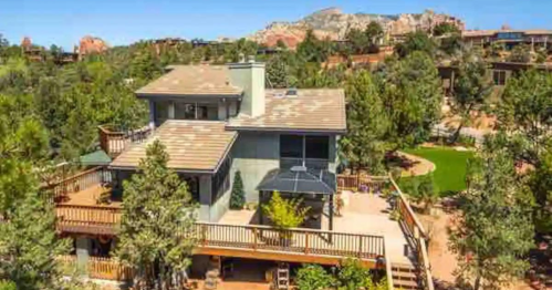 Aerial view of a modern house surrounded by trees and a landscaped yard, with mountains in the background.