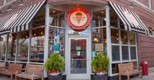 Exterior of an ice cream shop with a striped awning, bright signage, and benches outside. Warm, inviting atmosphere.