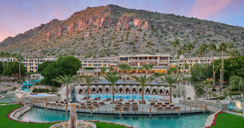 A luxurious resort with palm trees, a pool, and a mountain backdrop at sunset.