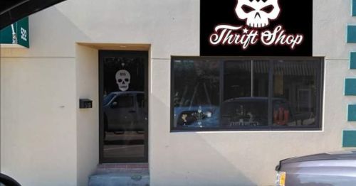 A thrift shop with a skull logo above the entrance, featuring a glass door and a simple exterior.
