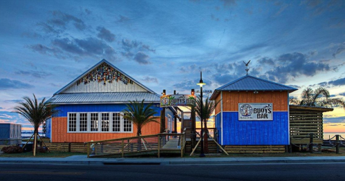 Colorful beach bar with palm trees, wooden deck, and a vibrant sunset sky in the background.