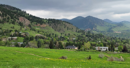 A scenic view of green hills and mountains under a cloudy sky, with houses nestled among trees in the foreground.