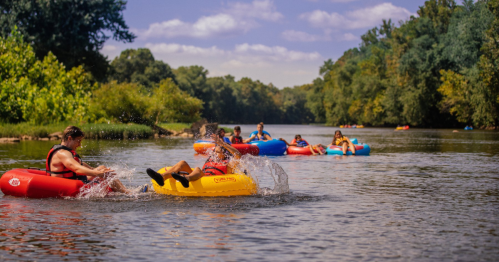 People floating on colorful inner tubes in a river, surrounded by lush greenery and a clear blue sky.