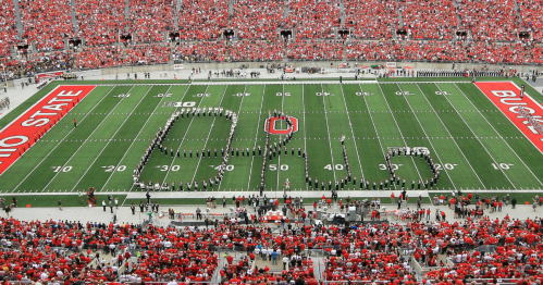 A large crowd in red fills a stadium as a marching band forms "O-H-I-O" on the football field.