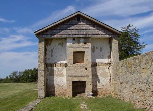 Historic building with a weathered stone facade, featuring a gabled roof and remnants of plaster, set against a blue sky.