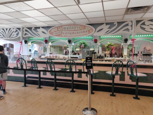 Interior of an ice cream shop with a counter, mirrors, and decorative lights. Empty stools line the counter.