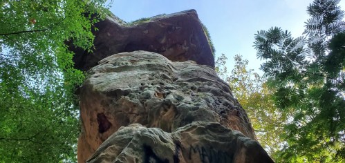 A towering rock formation surrounded by lush green trees under a clear blue sky.