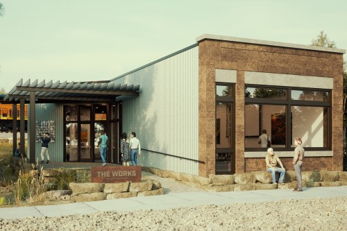 A modern building with large windows, featuring people outside and a sign reading "The Works." Surrounded by greenery.