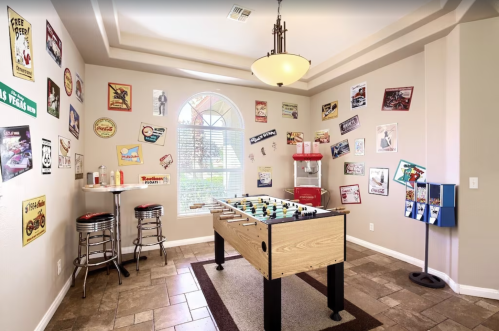 A game room featuring a foosball table, bar stools, and vintage posters on the walls.