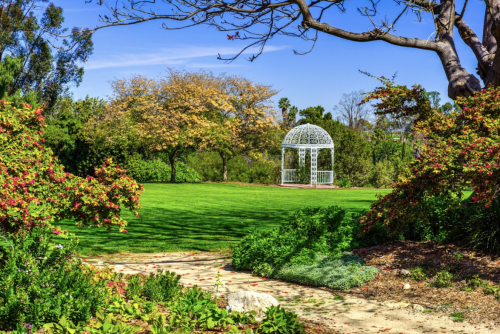 A serene garden with a white gazebo surrounded by lush greenery and colorful trees under a clear blue sky.