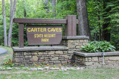 Sign for Carter Caves State Resort Park, featuring stone structure and surrounded by greenery and flowers.