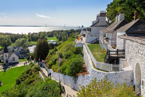 A scenic view of a coastal landscape with white buildings, greenery, and a bridge in the distance under a clear blue sky.