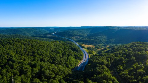 Aerial view of a winding highway through lush green hills under a clear blue sky.