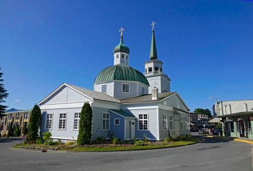 A white church with a green dome and spires, surrounded by trees and a clear blue sky.