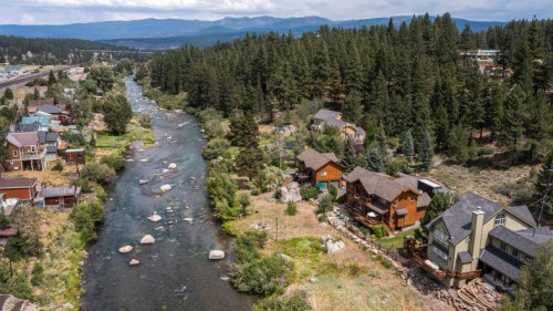 Aerial view of a river winding through a forested area with houses along the banks and mountains in the background.
