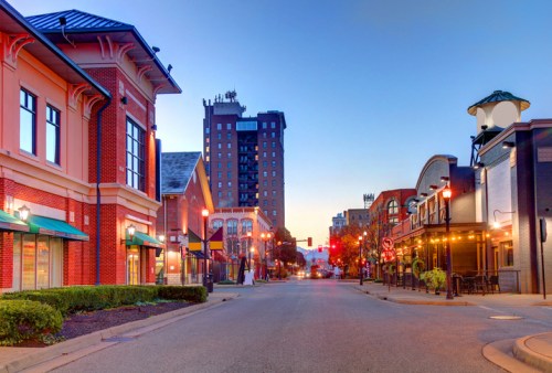Quiet urban street at dawn, lined with buildings and shops, with a tall hotel in the background.