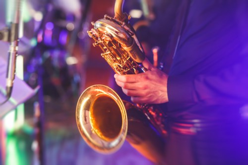 A close-up of a musician's hand holding a saxophone, with colorful stage lights in the background.
