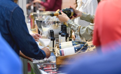 A person pours champagne into a glass at a wine tasting event, with bottles and ice in the background.