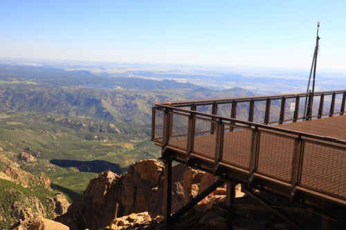 A viewing platform overlooking a vast mountainous landscape under a clear blue sky.