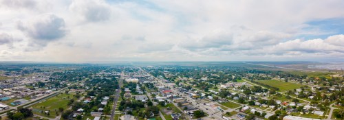 Aerial view of a small town with a grid layout, surrounded by fields and a cloudy sky.