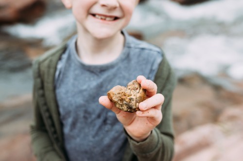 A smiling child holds a rock in front of a blurred natural background, showcasing excitement and curiosity.