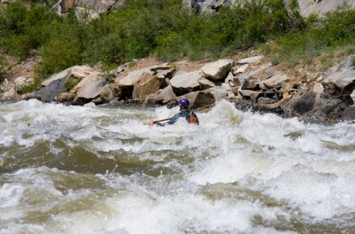 A kayaker navigates through turbulent whitewater rapids near rocky riverbanks.