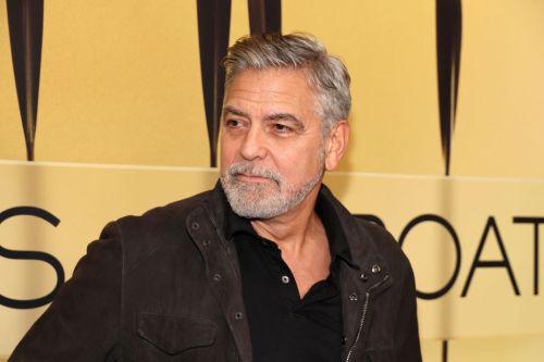 A man with gray hair and a beard, wearing a black jacket, poses against a yellow backdrop.