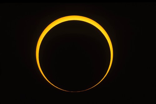 A bright, glowing crescent of the sun against a dark background, depicting a solar eclipse.