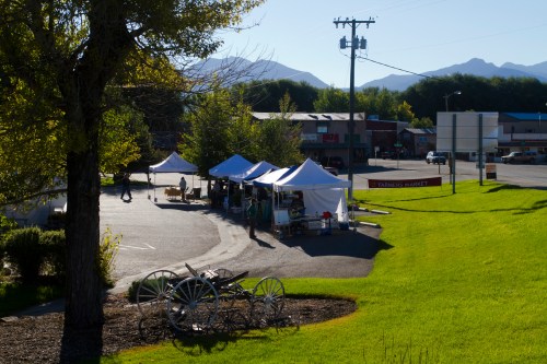 A sunny market scene with white tents, green grass, and mountains in the background. A vintage wagon is in the foreground.