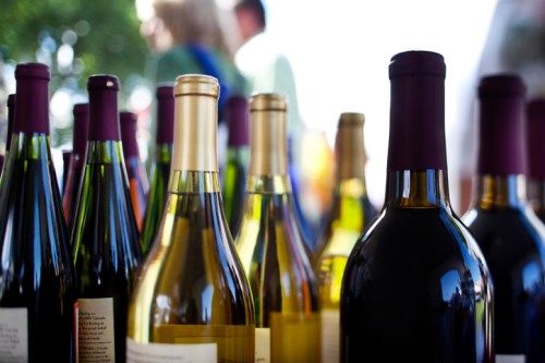 A close-up of various wine bottles with colorful labels, set against a blurred outdoor background.