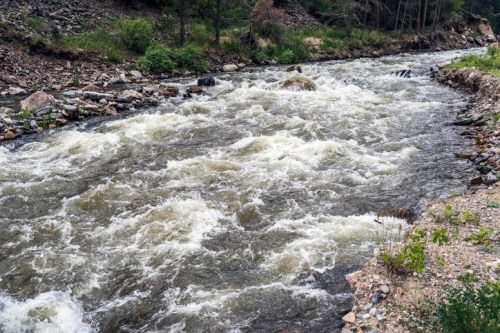 A rushing river flows through a rocky landscape, surrounded by greenery and trees.
