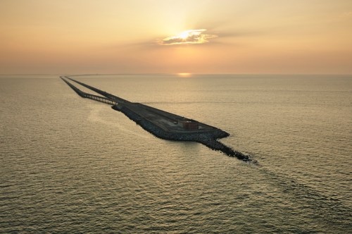 A long pier extends into calm waters under a golden sunset, with soft clouds in the sky.