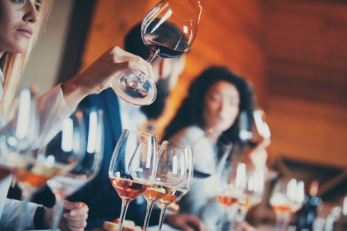 A group of people toasting with wine glasses at a social gathering, with various wine glasses in the foreground.