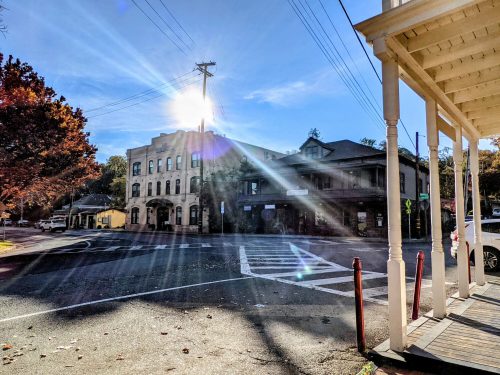 A sunbeam shines over a street intersection with historic buildings and trees, captured on a clear day.