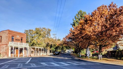 A quaint street scene with a saloon, colorful autumn trees, and clear blue skies.