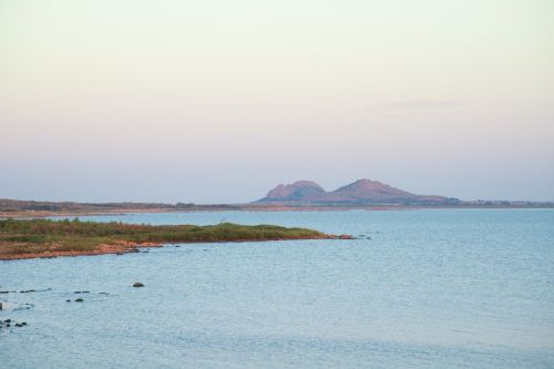 A serene view of a calm sea with distant hills under a pastel sky at dusk.