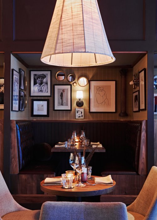 Cozy restaurant booth with framed art, a large lamp, and elegantly set tables, creating an inviting atmosphere.