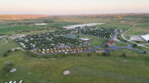 Aerial view of a green landscape with a campground, trees, and rolling hills in the background during sunset.