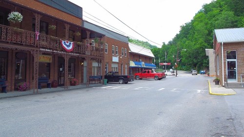 A quiet street scene featuring brick buildings, parked trucks, and greenery in the background.