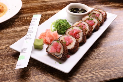 A plate of sushi rolls with tuna, served with wasabi, pickled ginger, and soy sauce on a wooden table.