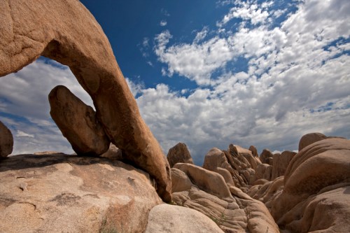 A rocky landscape with large boulders under a cloudy sky, featuring a prominent arch-shaped rock formation.